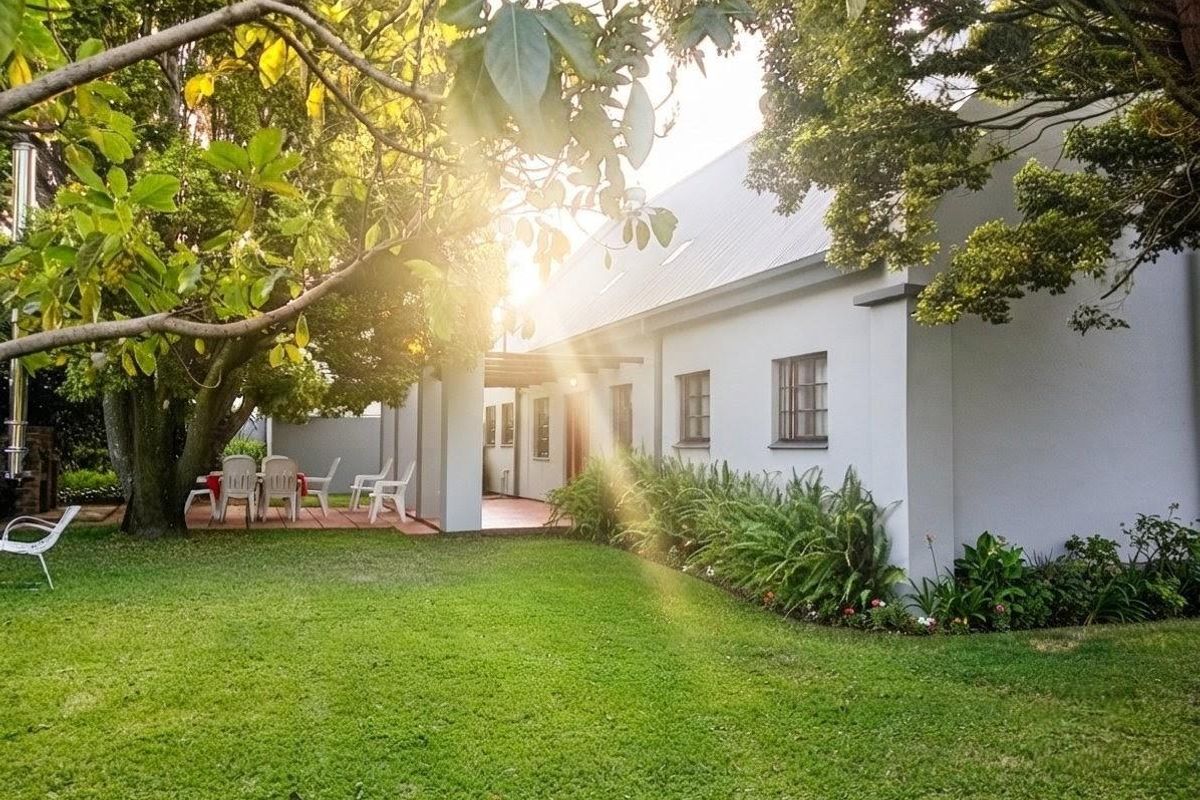 A view of the rear exterior of the house featuring a tiled patio area, well-maintained lawn, and mature garden landscaping.