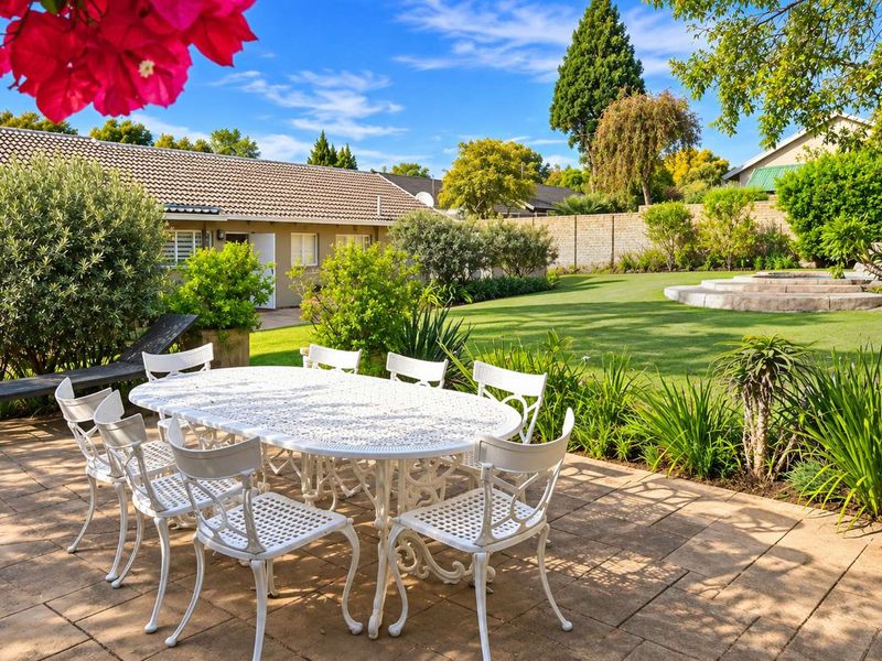 A well-maintained rear garden featuring a paved patio area, lush lawn, and established landscaping, providing a private outdoor space for relaxation.