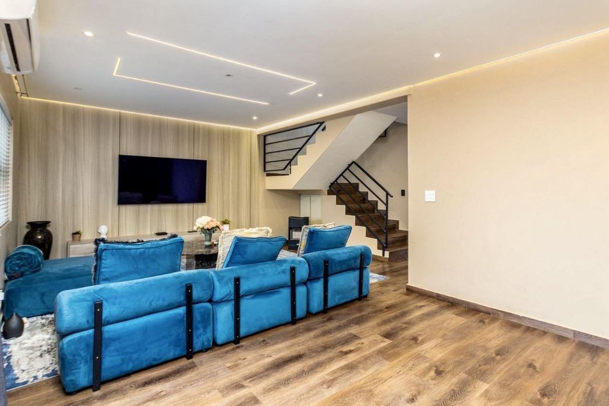 Modern living room featuring wood-look flooring, a stylish wood-panelled feature wall with integrated lighting, and an open staircase with a contemporary metal railing.