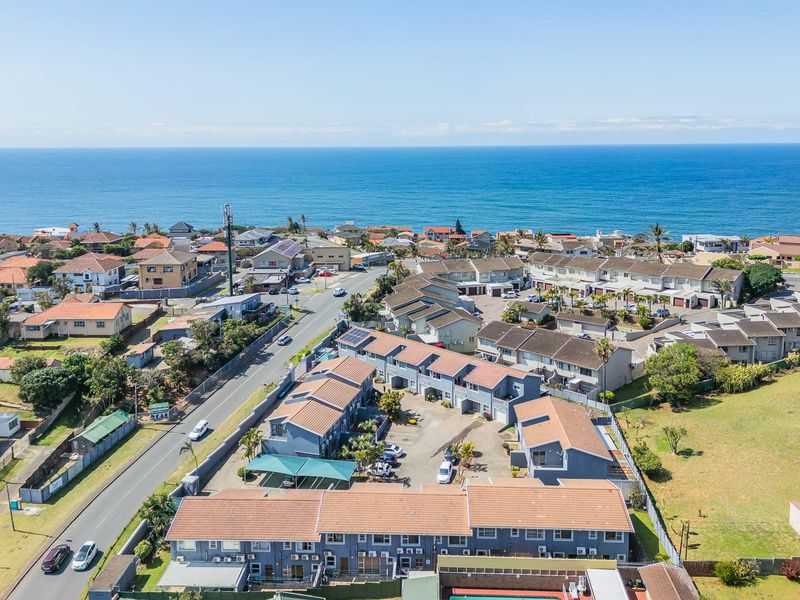 Aerial view of a coastal apartment complex featuring tiled roofs, paved parking areas, and proximity to the ocean.
