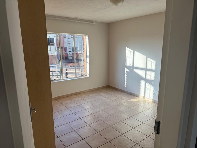 A vacant bedroom featuring neutral tiled flooring, a window with security bars, and plain walls, offering a blank canvas for personalization.
