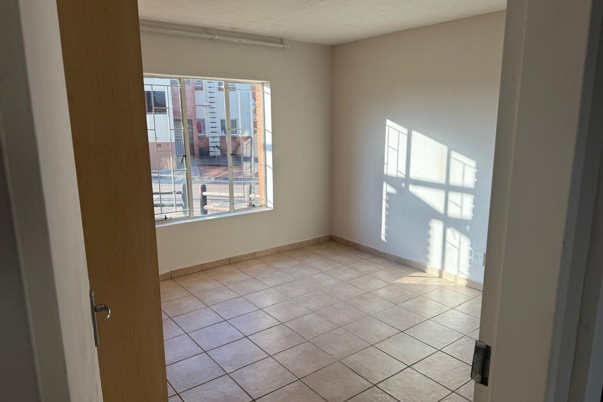 A vacant bedroom featuring neutral tiled flooring, a window with security bars, and plain walls, offering a blank canvas for personalization.