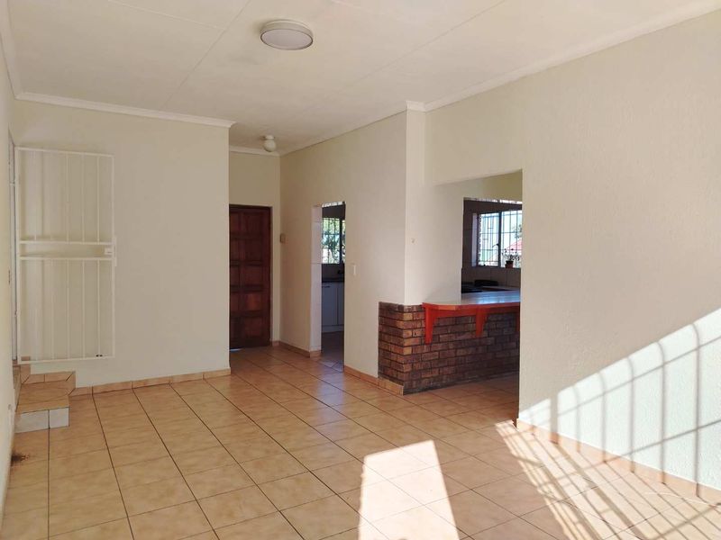 An open-plan living area featuring tiled flooring, a brick breakfast bar, and direct access to adjacent rooms, offering a blank canvas for interior design.