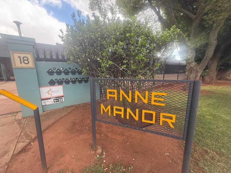 Entrance view of Anne Manor townhouse complex featuring security signage, post boxes, and perimeter fencing.