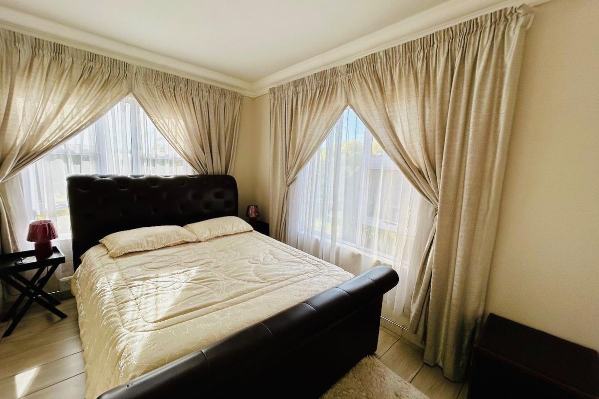 A well-lit bedroom featuring tiled flooring, corner windows with fitted curtains, and crown molding.