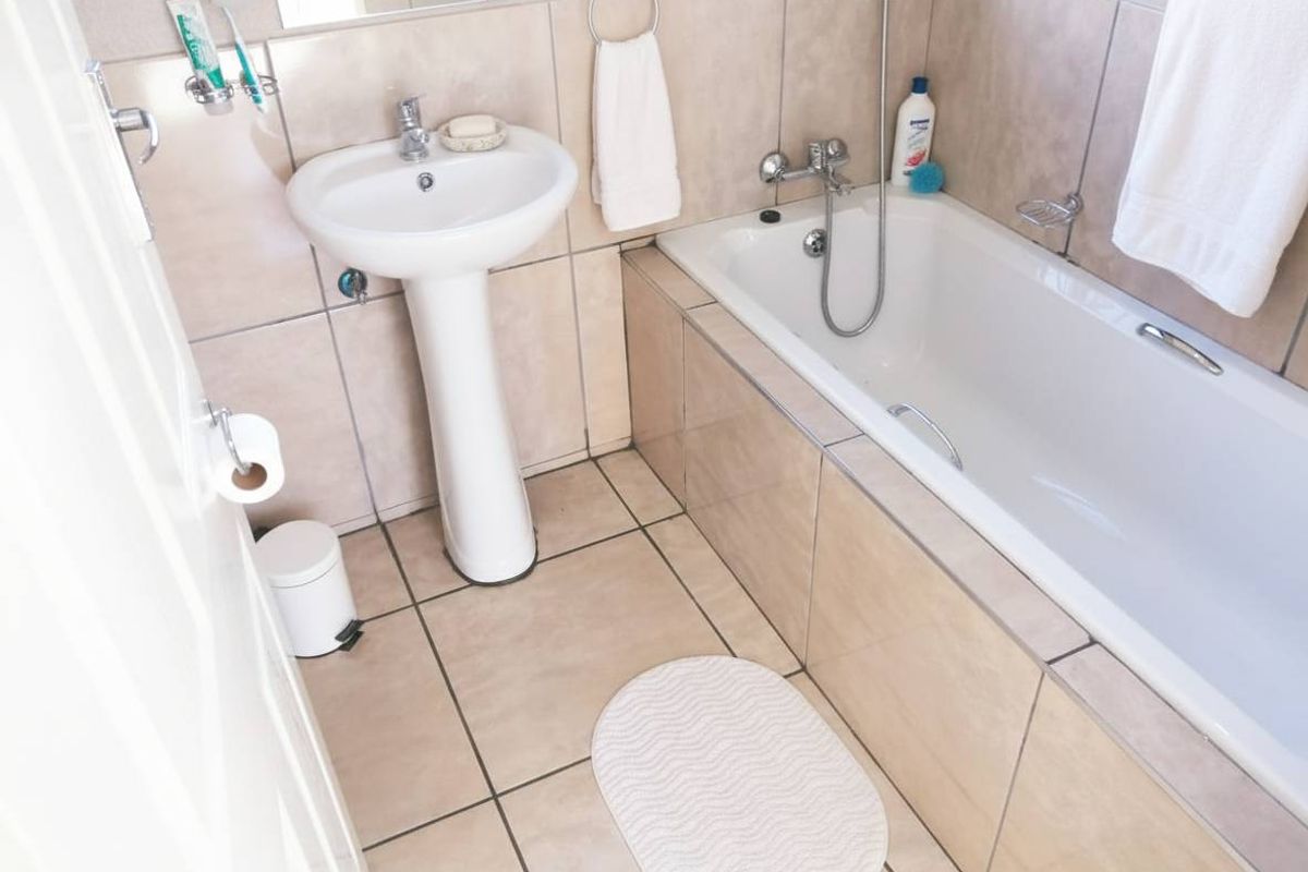 A functional bathroom featuring a pedestal basin, tiled walls and flooring, and a built-in bathtub with chrome fixtures.
