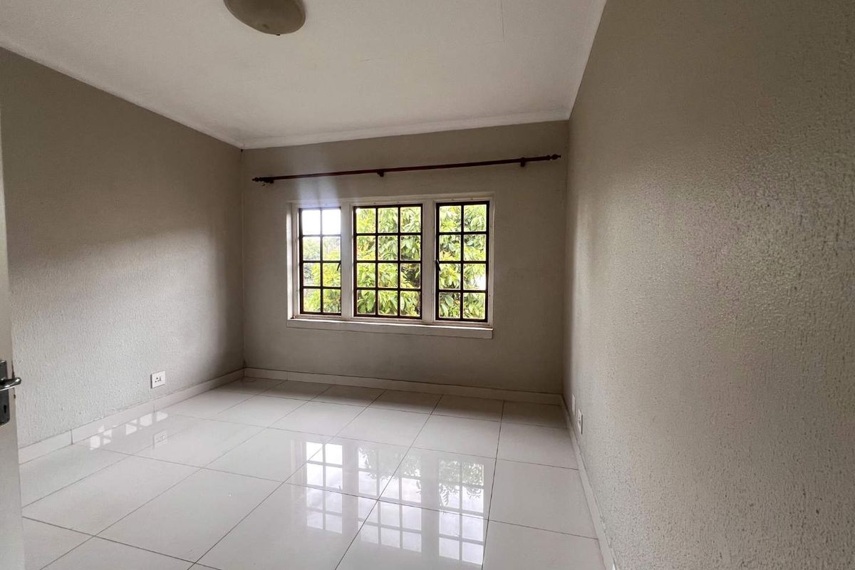 A bright, empty bedroom featuring neutral walls, polished tiled flooring, and a classic grid-pattern window with a curtain rod installed.