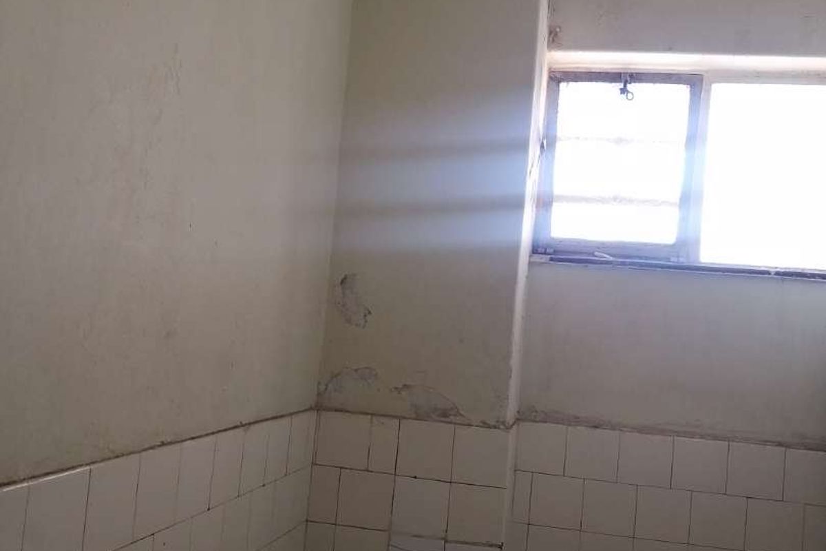 A dated bathroom interior featuring wall tiling and a window, currently showing significant signs of wear and requiring renovation.