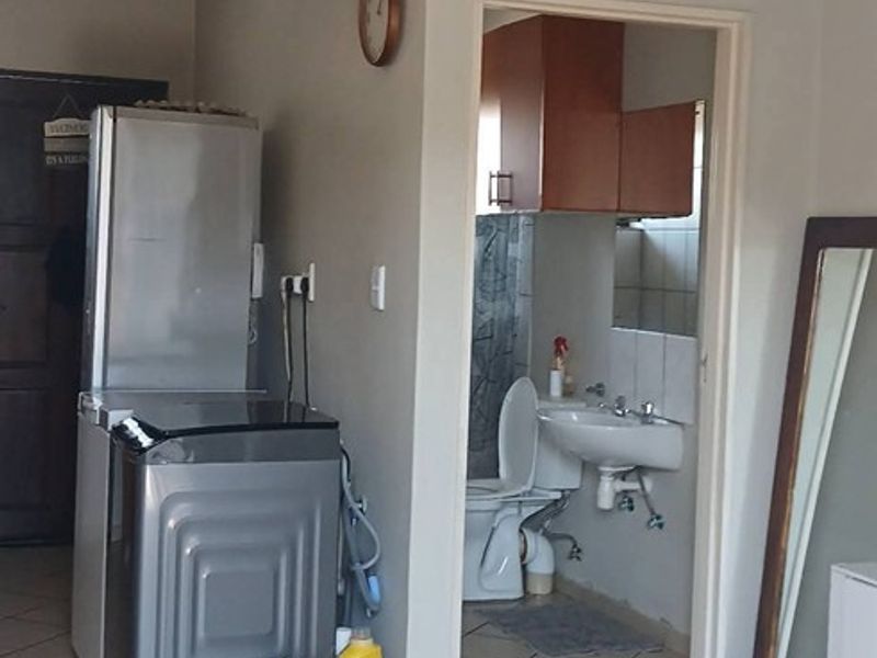 A utility area featuring tiled flooring and plumbing connections, with an adjacent bathroom containing a toilet and vanity.