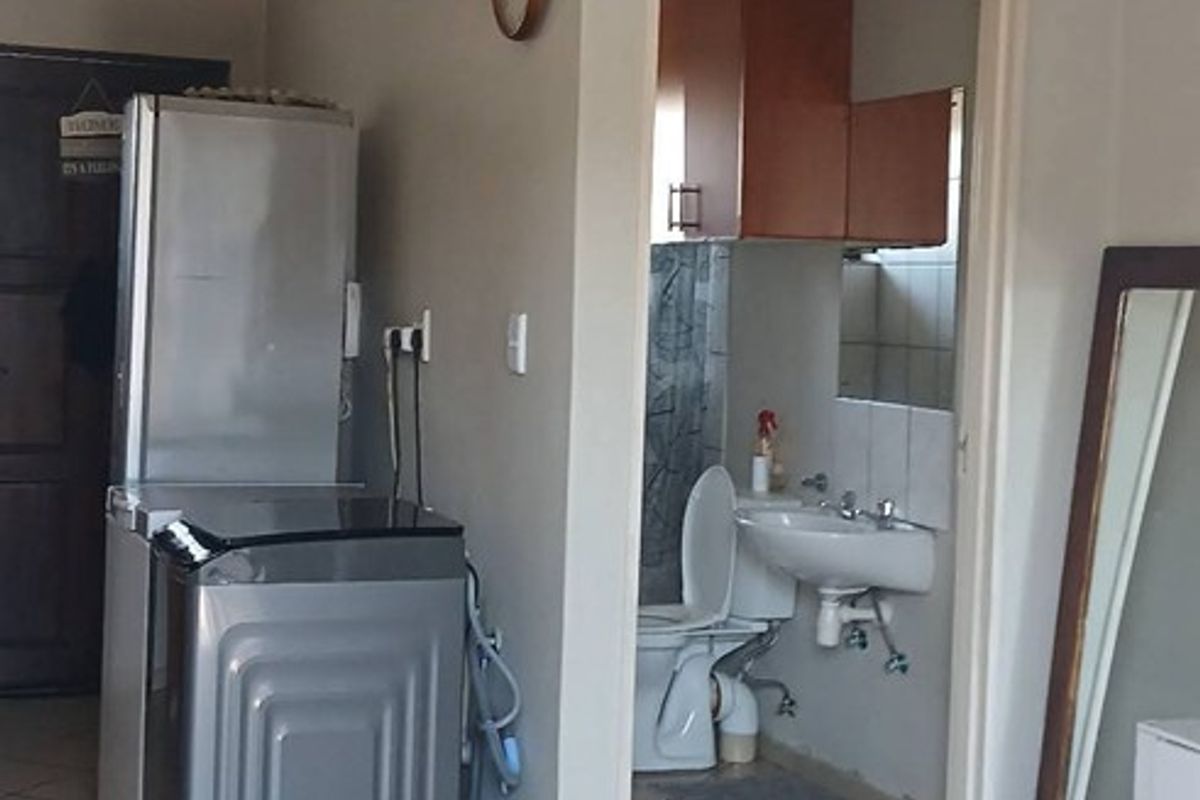 A utility area featuring tiled flooring and plumbing connections, with an adjacent bathroom containing a toilet and vanity.