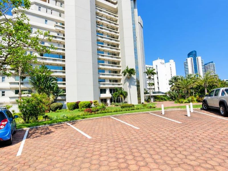 Exterior view of a modern multi-story apartment complex featuring a paved parking area and well-maintained landscaped grounds.