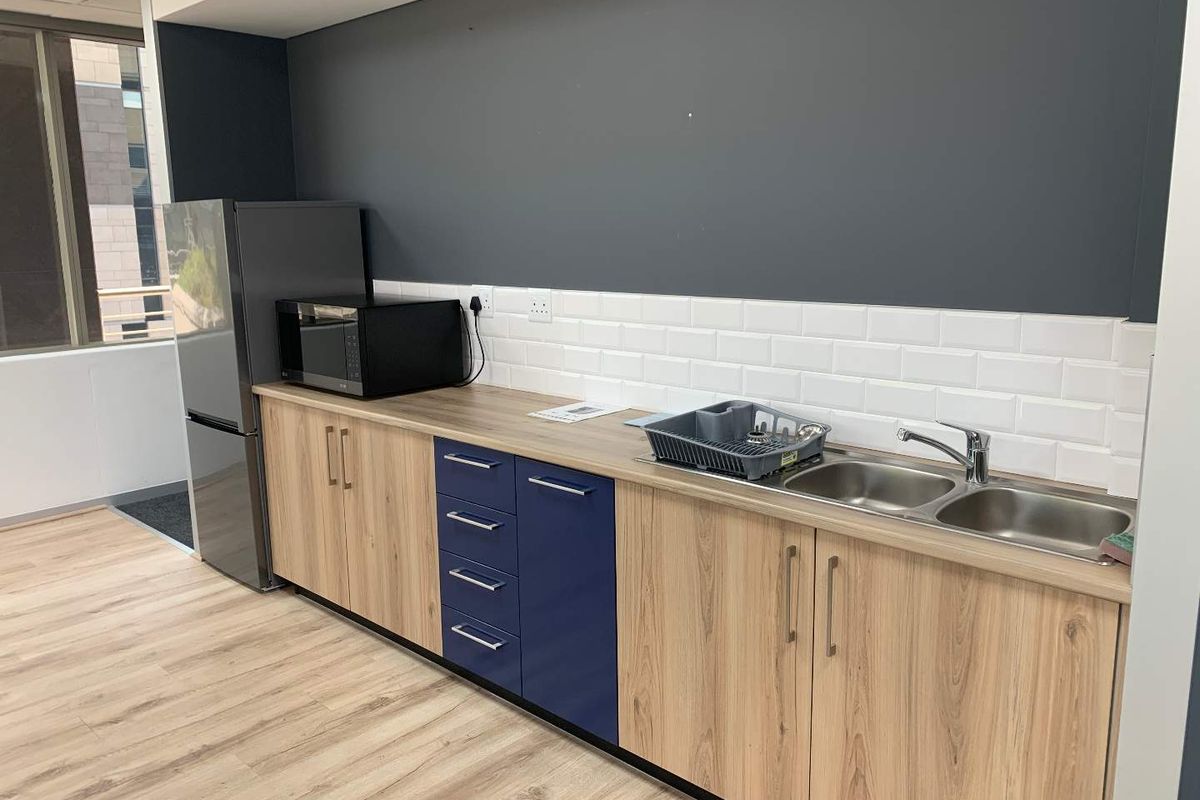 A modern office kitchenette featuring wood-look laminate cabinetry, a subway tile backsplash, and a double bowl stainless steel sink with a mixer tap.