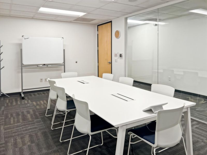 A professional office meeting room featuring a large conference table, glass partition wall, suspended ceiling, and durable carpet tile flooring.