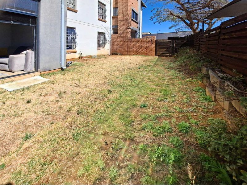 A private rear garden area featuring a lawn, brick boundary walls, and timber fencing, accessible via a sliding glass door from the living space.
