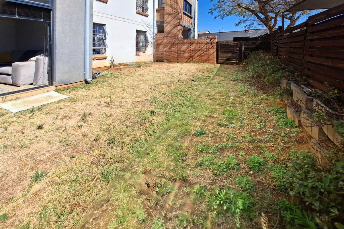 A private rear garden area featuring a lawn, brick boundary walls, and timber fencing, accessible via a sliding glass door from the living space.