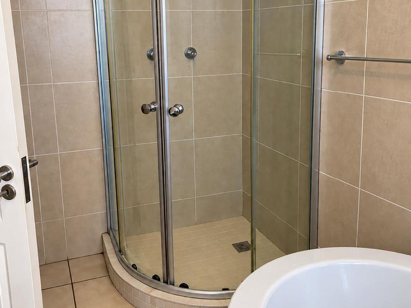 A functional bathroom featuring a curved glass shower enclosure with tiled walls and flooring, providing a clean and practical layout.