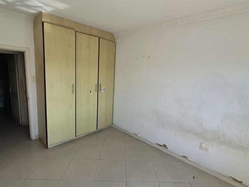 An empty bedroom featuring built-in cupboards, tiled flooring, and decorative cornice, requiring cosmetic wall repairs and painting to restore its condition.
