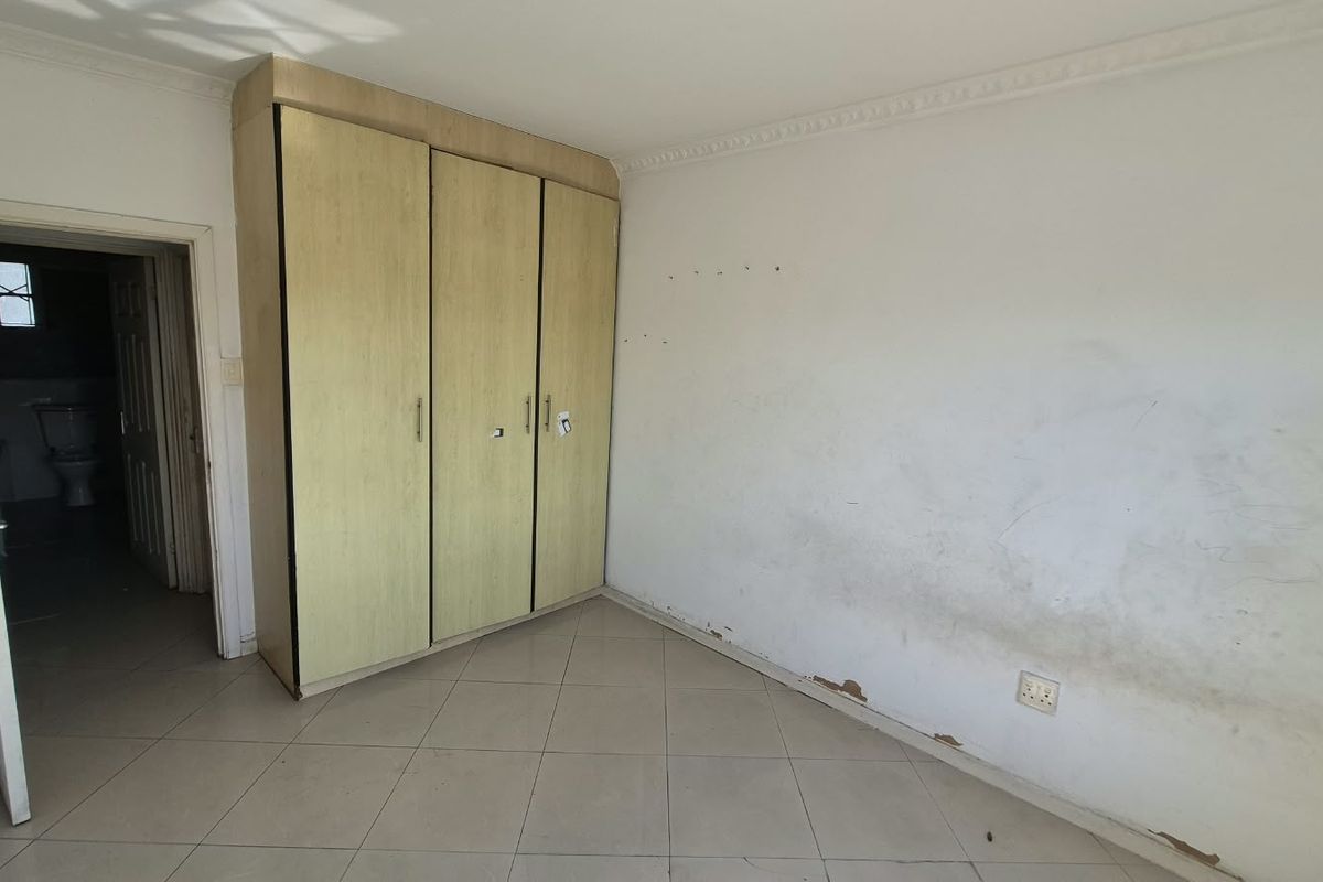 An empty bedroom featuring built-in cupboards, tiled flooring, and decorative cornice, requiring cosmetic wall repairs and painting to restore its condition.