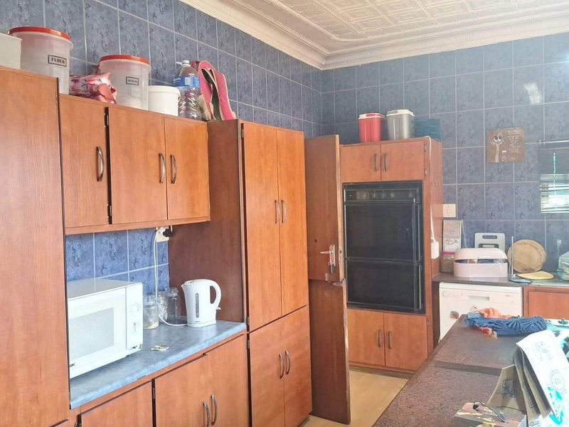 A dated kitchen featuring wood-finish cabinetry, built-in oven, hob, and blue wall tiling, offering potential for a modern renovation.