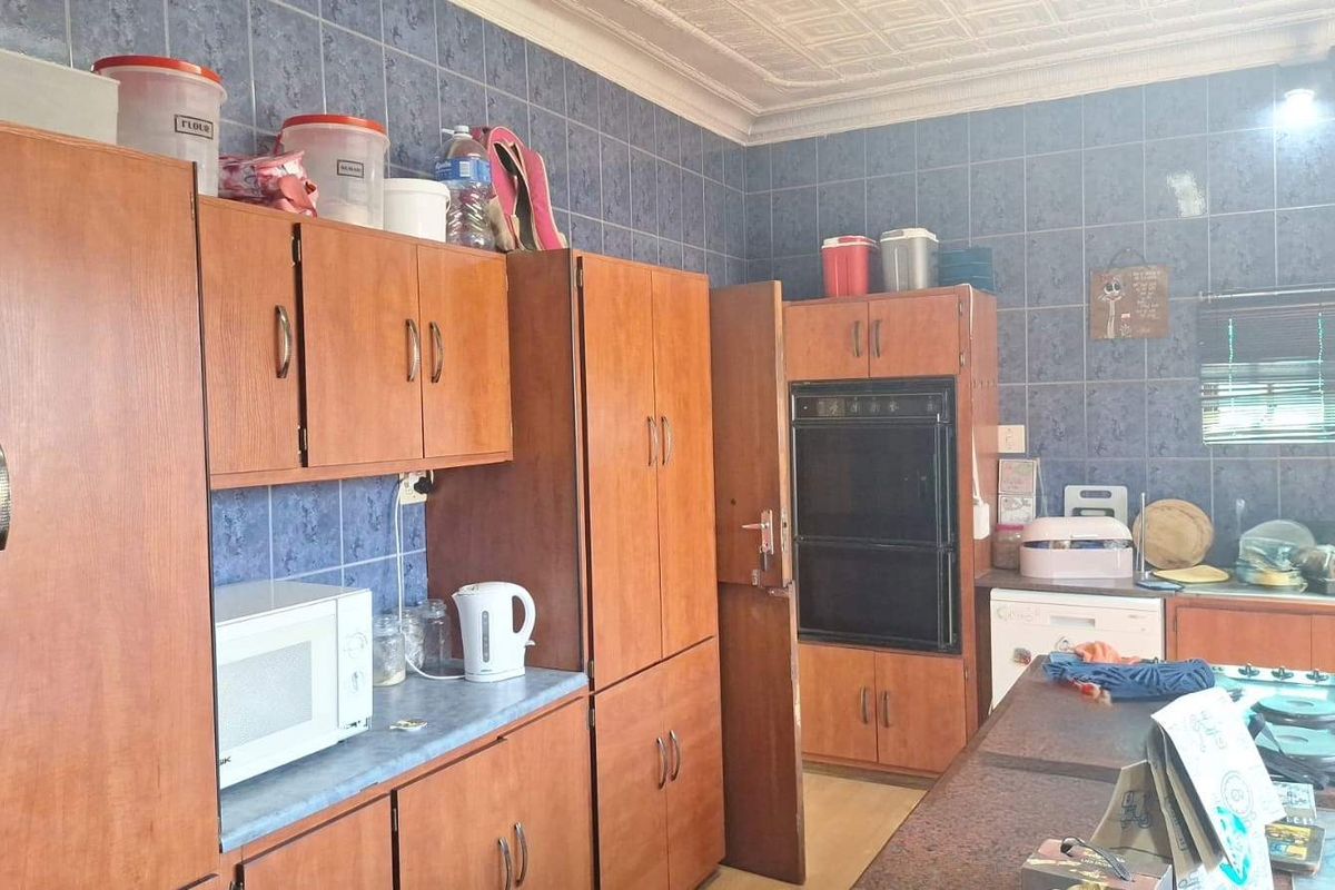 A dated kitchen featuring wood-finish cabinetry, built-in oven, hob, and blue wall tiling, offering potential for a modern renovation.