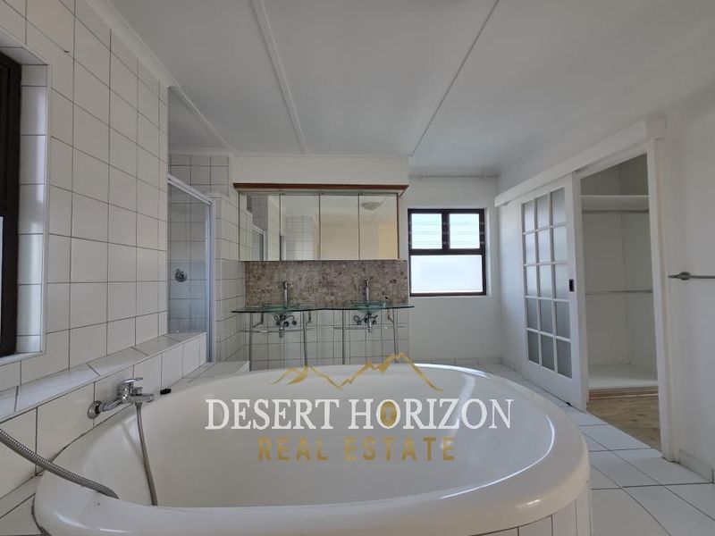 Spacious bathroom featuring a large soaking tub, double vanity with glass sinks, walk-in shower, and an integrated walk-in closet area.