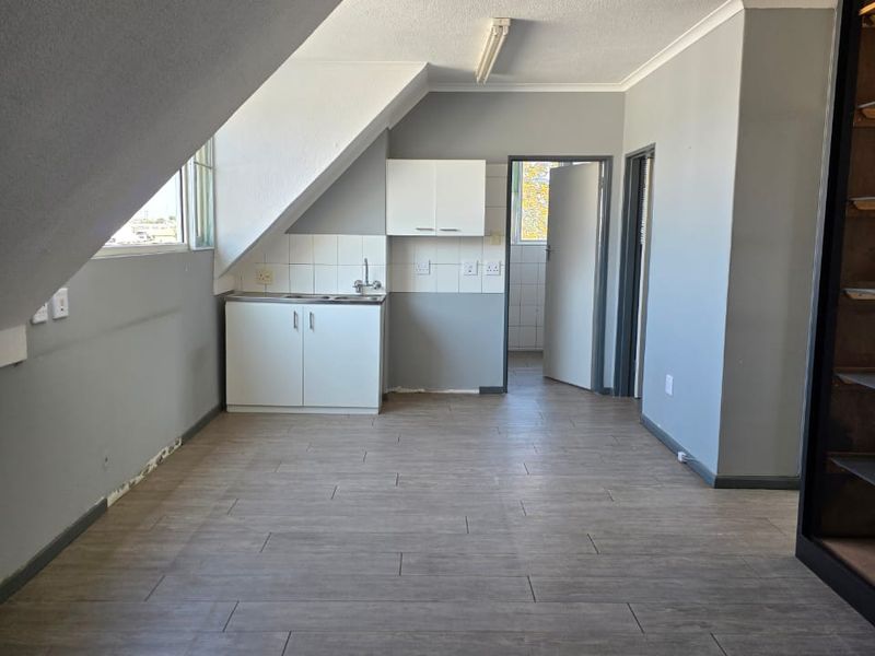 An empty kitchen area featuring built-in cabinetry, a stainless steel sink, tiled splashback, and modern wood-look floor tiles under a sloped ceiling.