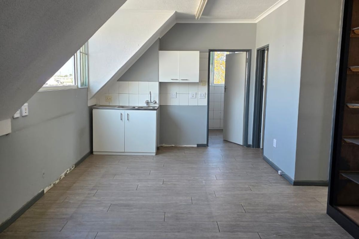 An empty kitchen area featuring built-in cabinetry, a stainless steel sink, tiled splashback, and modern wood-look floor tiles under a sloped ceiling.