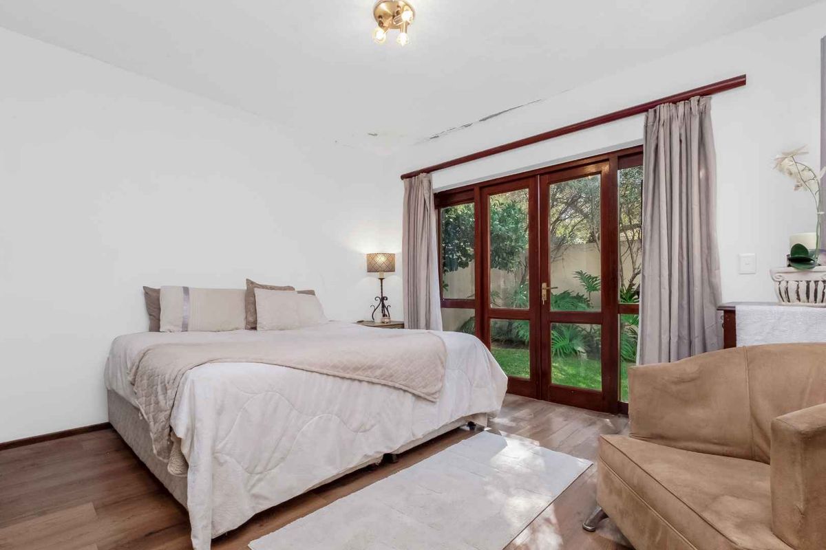 A bedroom featuring wooden flooring and timber-framed glass doors that open directly onto a private garden area.
