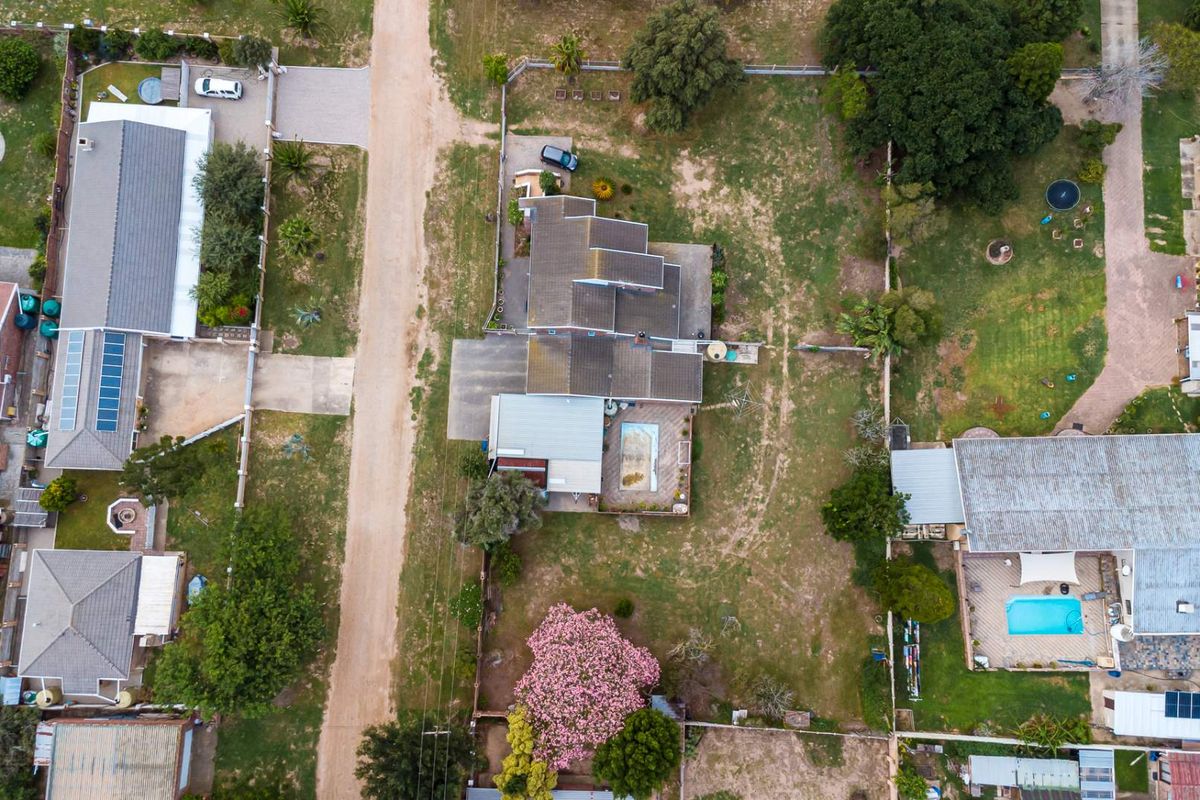 Aerial view of a residential property featuring a swimming pool, tiled roof structure, and surrounding garden space within a suburban neighborhood.