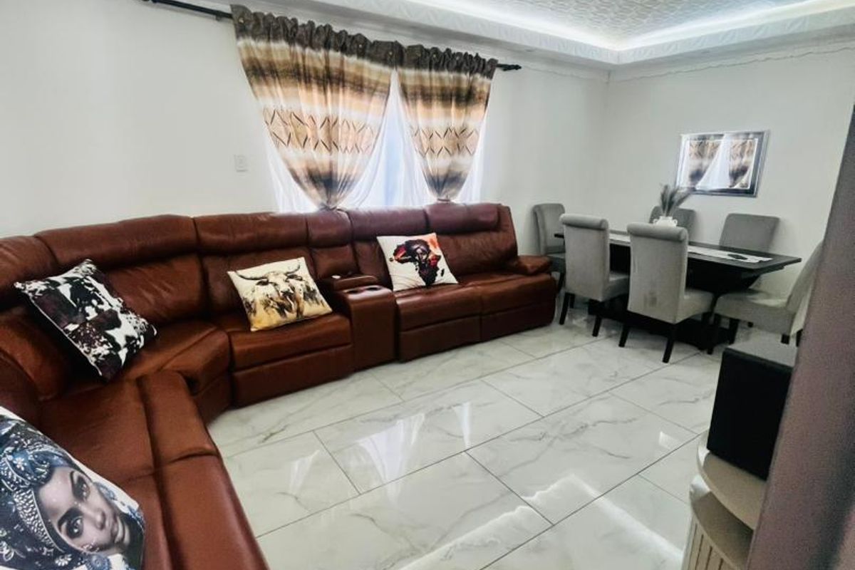 Open-plan living and dining area featuring large format marble-look floor tiles, a decorative textured ceiling, and modern recessed lighting.