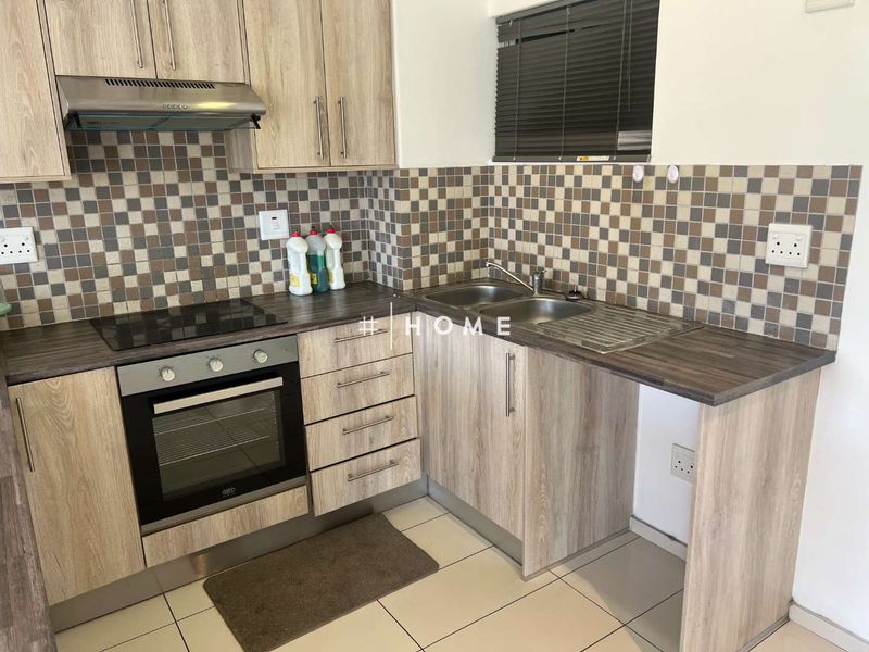 A functional kitchen featuring wood-look laminate cabinetry, mosaic tile backsplash, built-in oven with hob, and a stainless steel sink.