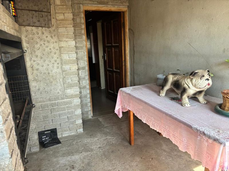 Covered patio area featuring a built-in brick braai and direct access to the home interior through a timber door.