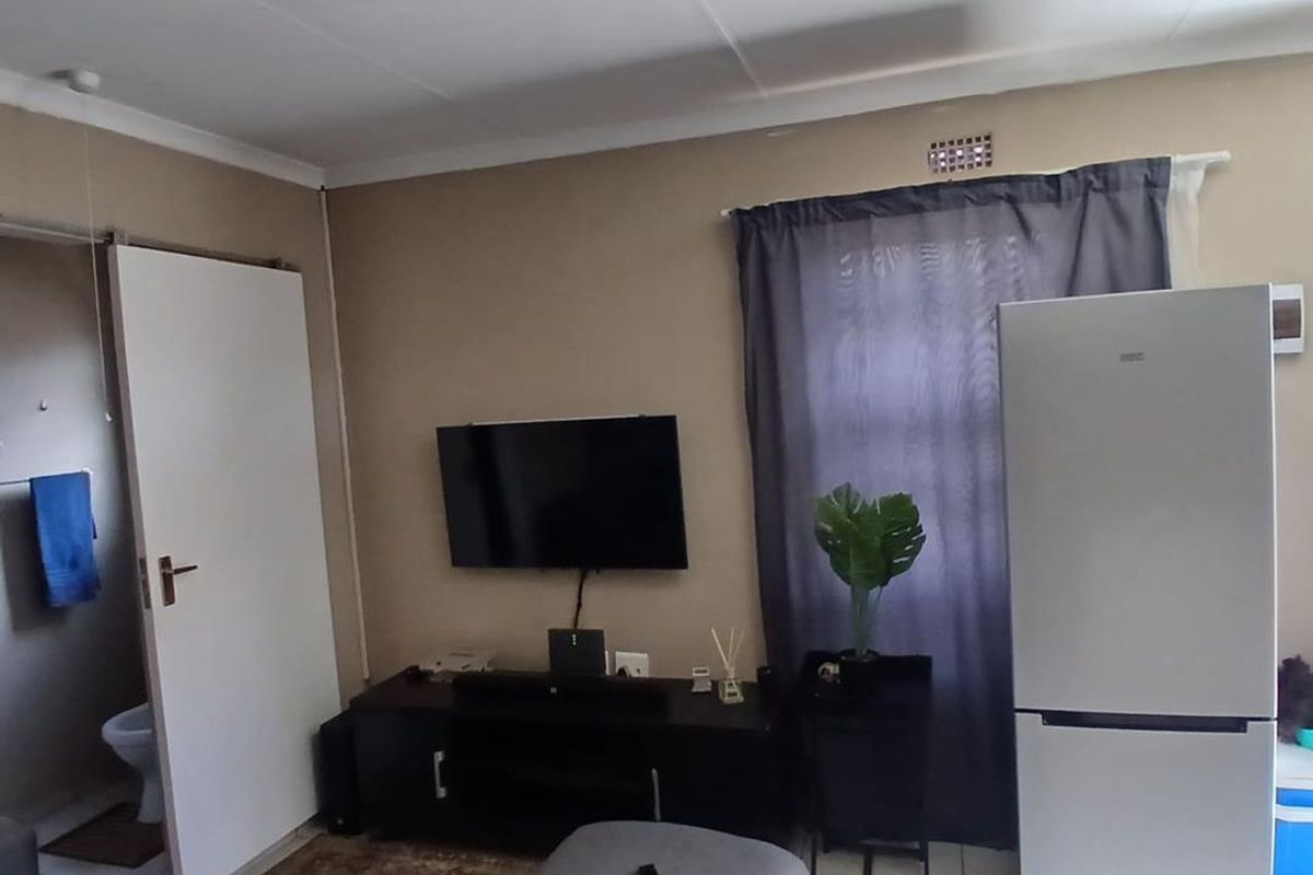 A living room area featuring tiled flooring, a wall-mounted television point, and direct access to an adjacent bathroom.