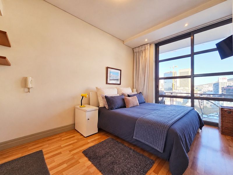 A well-maintained bedroom featuring hardwood flooring, recessed lighting, and large floor-to-ceiling windows that provide ample natural light and city views.