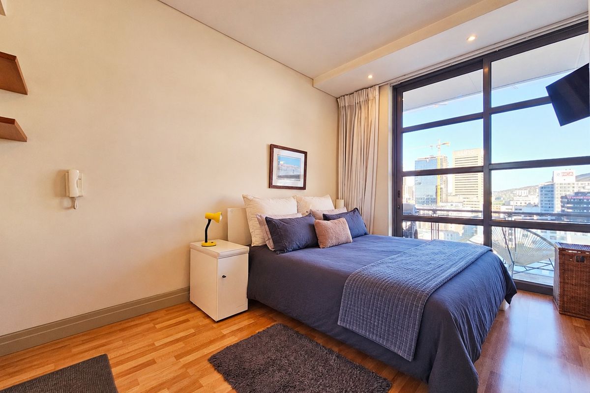 A well-maintained bedroom featuring hardwood flooring, recessed lighting, and large floor-to-ceiling windows that provide ample natural light and city views.