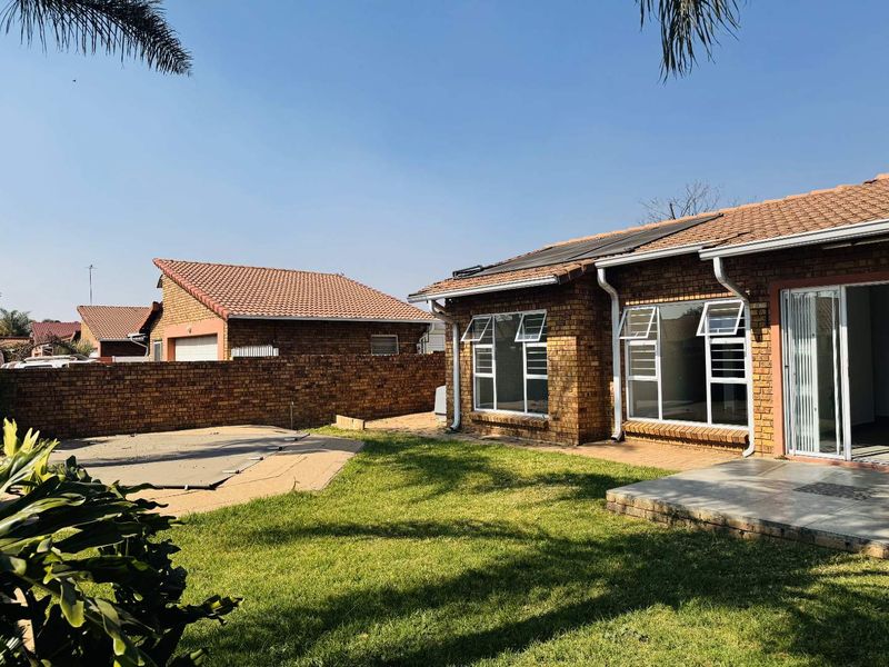 Rear view of a face brick cluster home featuring a private garden, swimming pool with cover, paved patio area, and solar water heating panels.