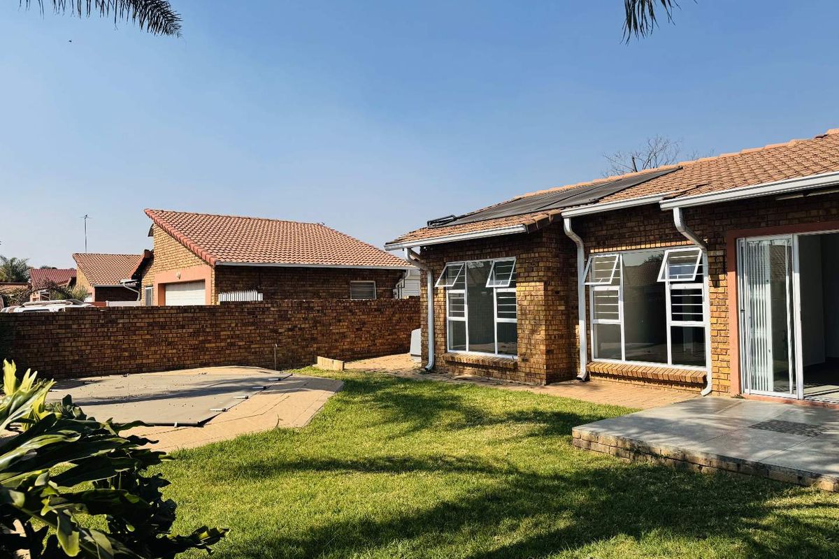 Rear view of a face brick cluster home featuring a private garden, swimming pool with cover, paved patio area, and solar water heating panels.