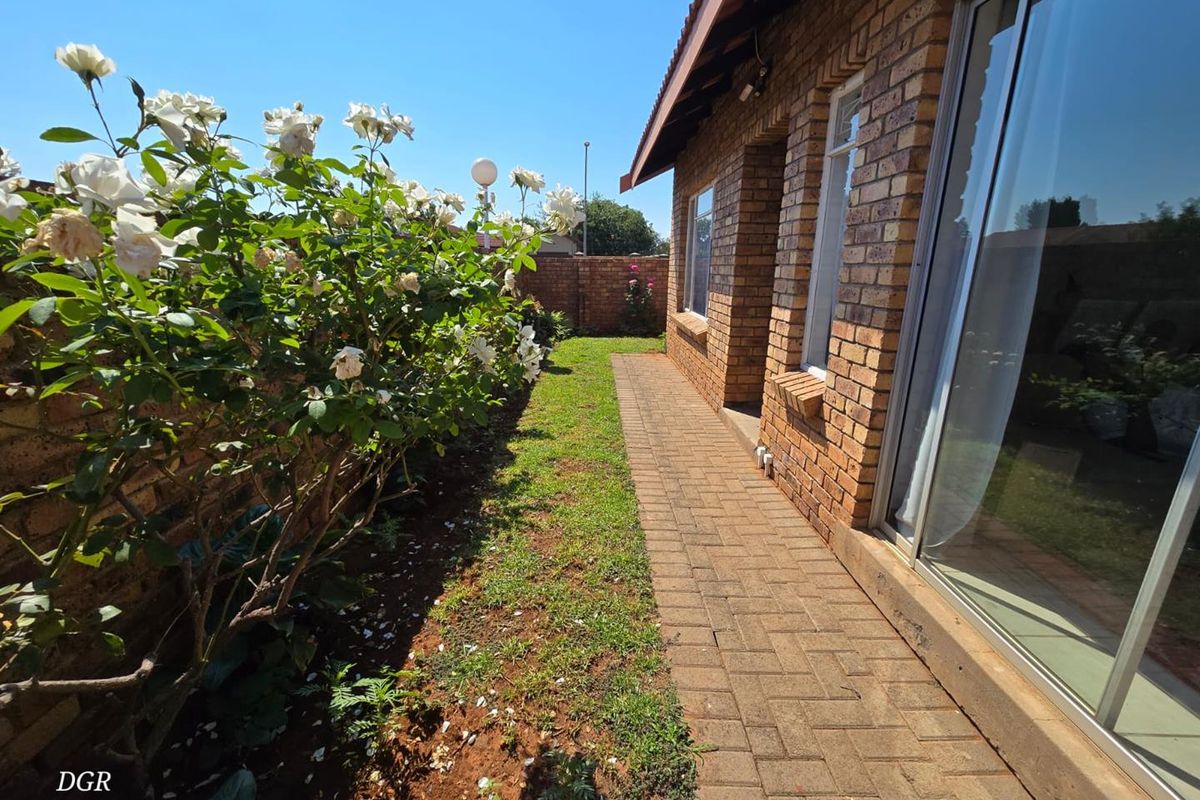 A well-maintained rear garden area featuring a paved walkway, brick exterior walls, and sliding glass doors leading into the townhouse.