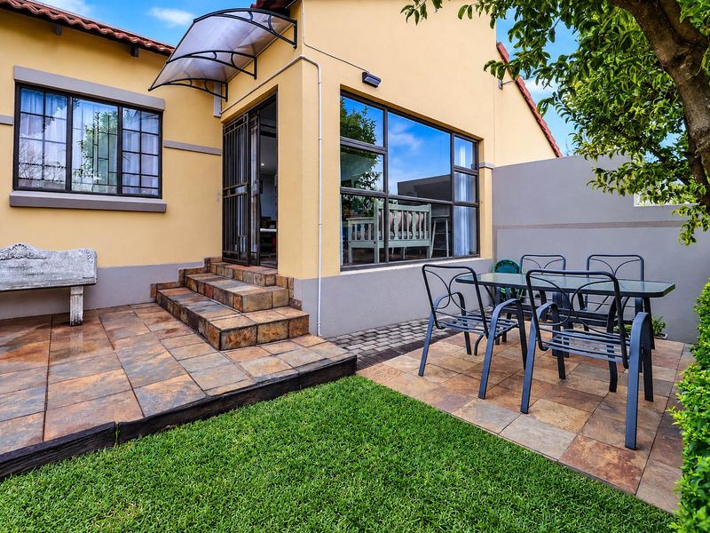 A well-maintained rear patio area featuring tiled flooring, a protective awning, and direct access to the interior through a security gate.