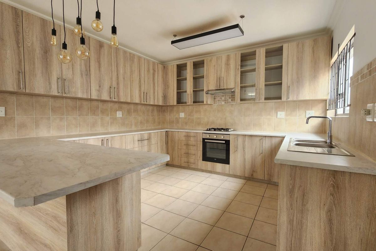 A well-maintained kitchen featuring light wood-grain cabinetry, stone-look countertops, a built-in oven and hob, and tiled flooring.