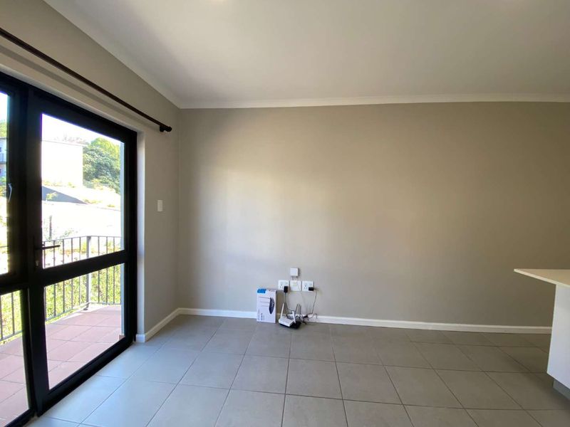 An empty living area featuring neutral tiled flooring, a sliding glass door leading to a balcony, and integrated electrical and data connectivity points.