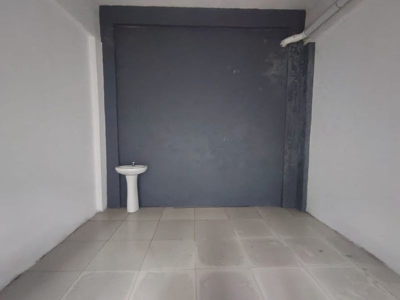 A vacant utility space featuring tiled flooring, a pedestal basin, and exposed plumbing, suitable for storage or a functional wash area.