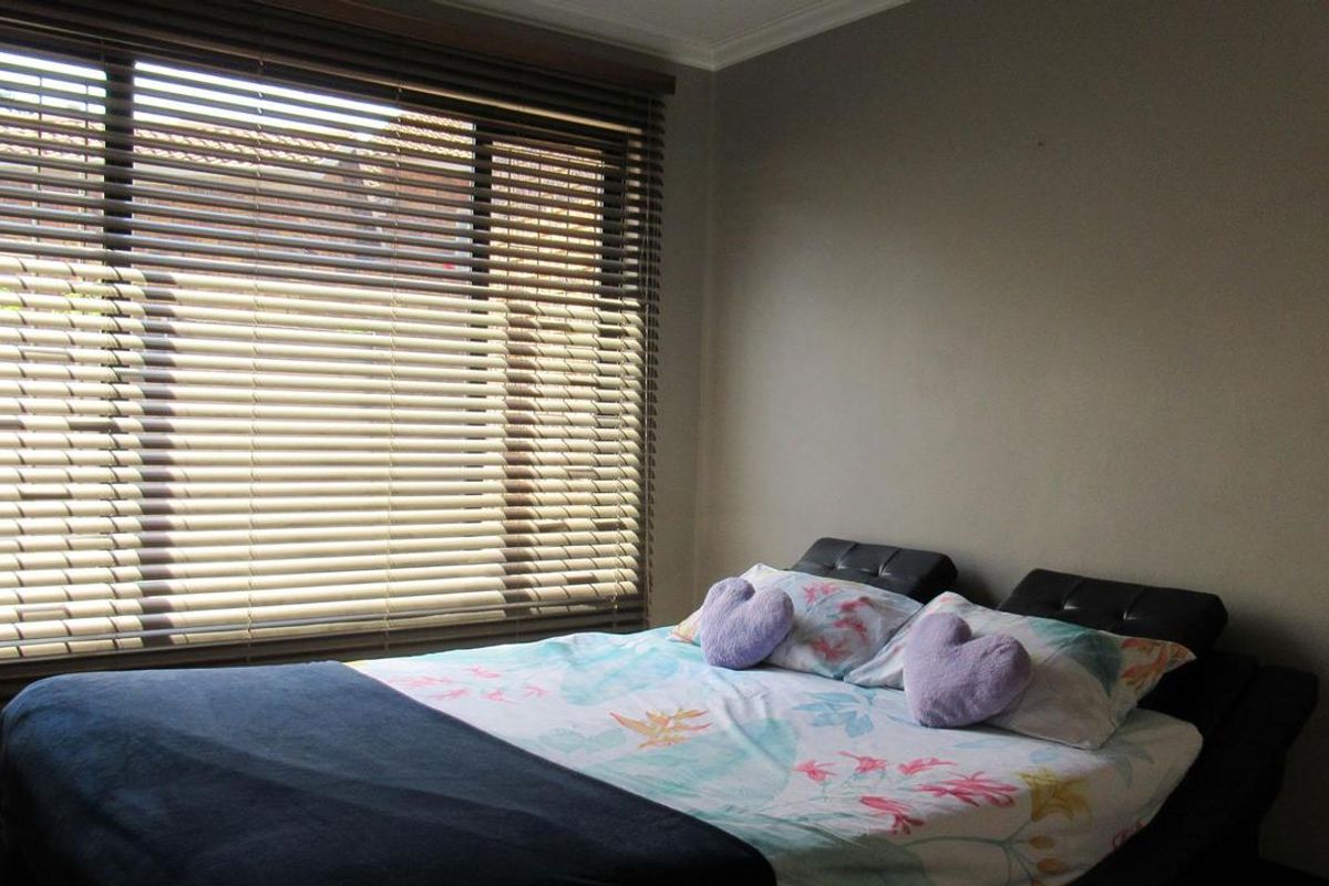 A bedroom featuring neutral wall tones and large windows fitted with horizontal blinds, providing natural light to the space.