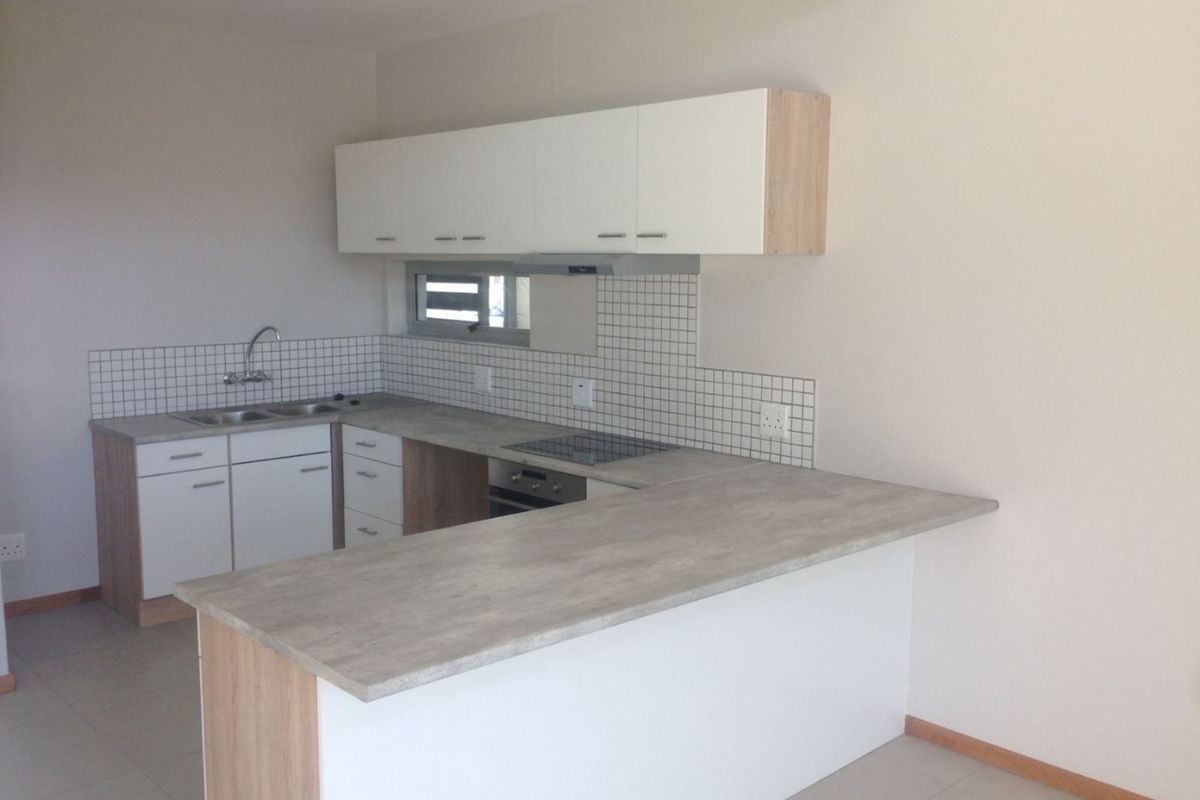 A modern kitchen featuring white cabinetry, wood-tone accents, a breakfast bar, built-in oven, and hob with a tiled splashback.