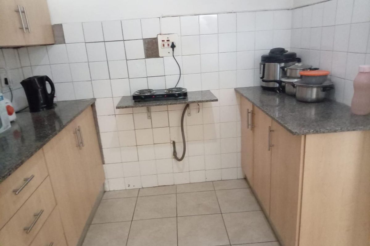 A compact kitchen featuring laminate cabinetry, granite countertops, and ceramic tiling, currently showing signs of wear and exposed utility piping.
