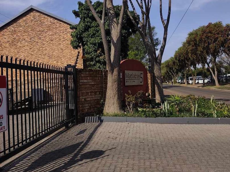 Entrance view of the Matlabas complex featuring a brick boundary wall, metal security gate, and paved driveway access.