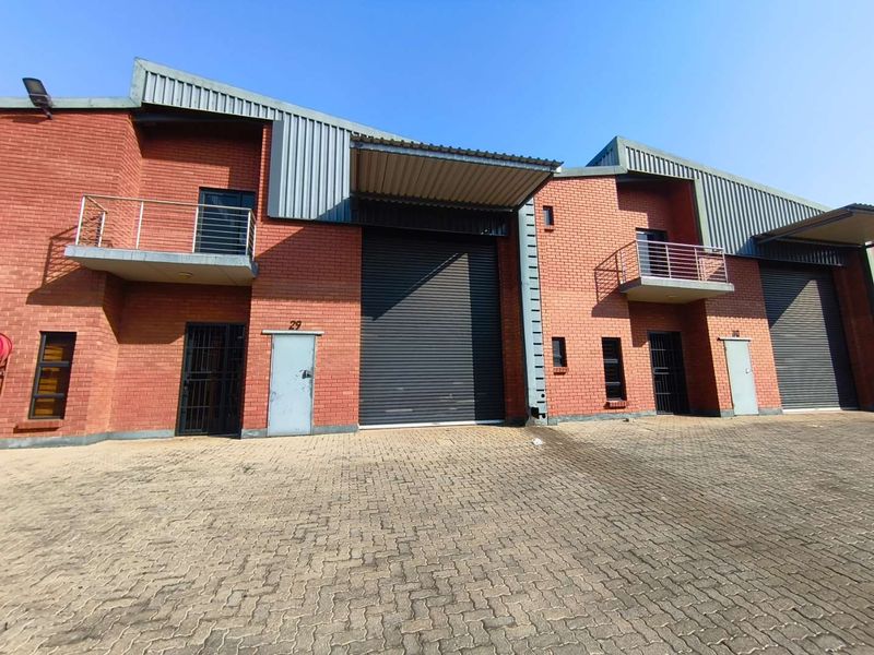 Front elevation of industrial warehouse units featuring red brick construction, large roller shutter doors, and upper-level balconies with steel railings.