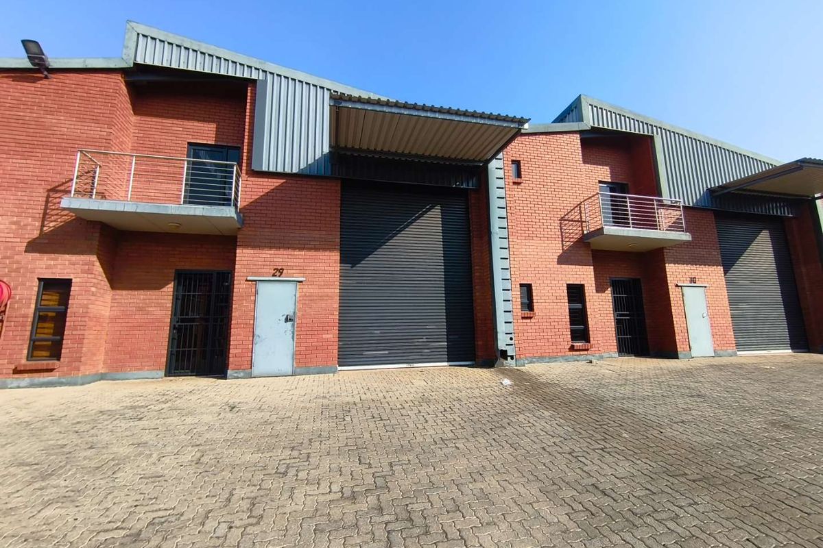 Front elevation of industrial warehouse units featuring red brick construction, large roller shutter doors, and upper-level balconies with steel railings.
