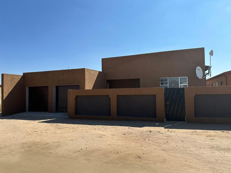 Front exterior view of a single-story house featuring a double garage, secure boundary wall, and gated entrance.
