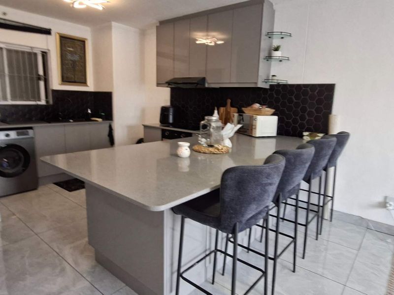 Modern kitchen featuring a central island with breakfast bar seating, sleek grey cabinetry, quartz countertops, and a stylish hexagonal tile backsplash.
